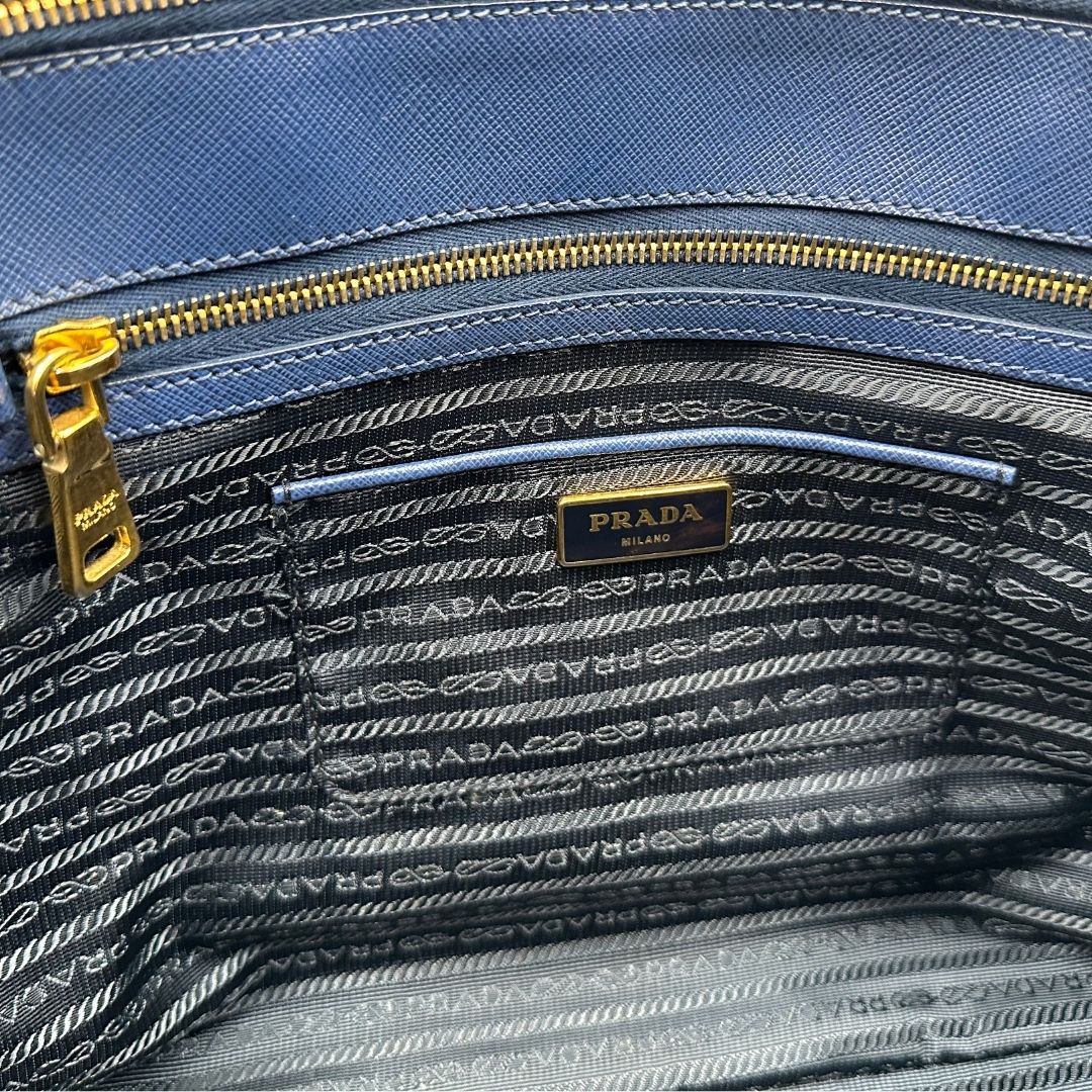 interno Borsa Prada in pelle saffiano blu con parti metalliche dorate; munita di doppi manici stondati e impreziosita da una clochette portachiavi, di lusso, originale, ottime condizioni. 