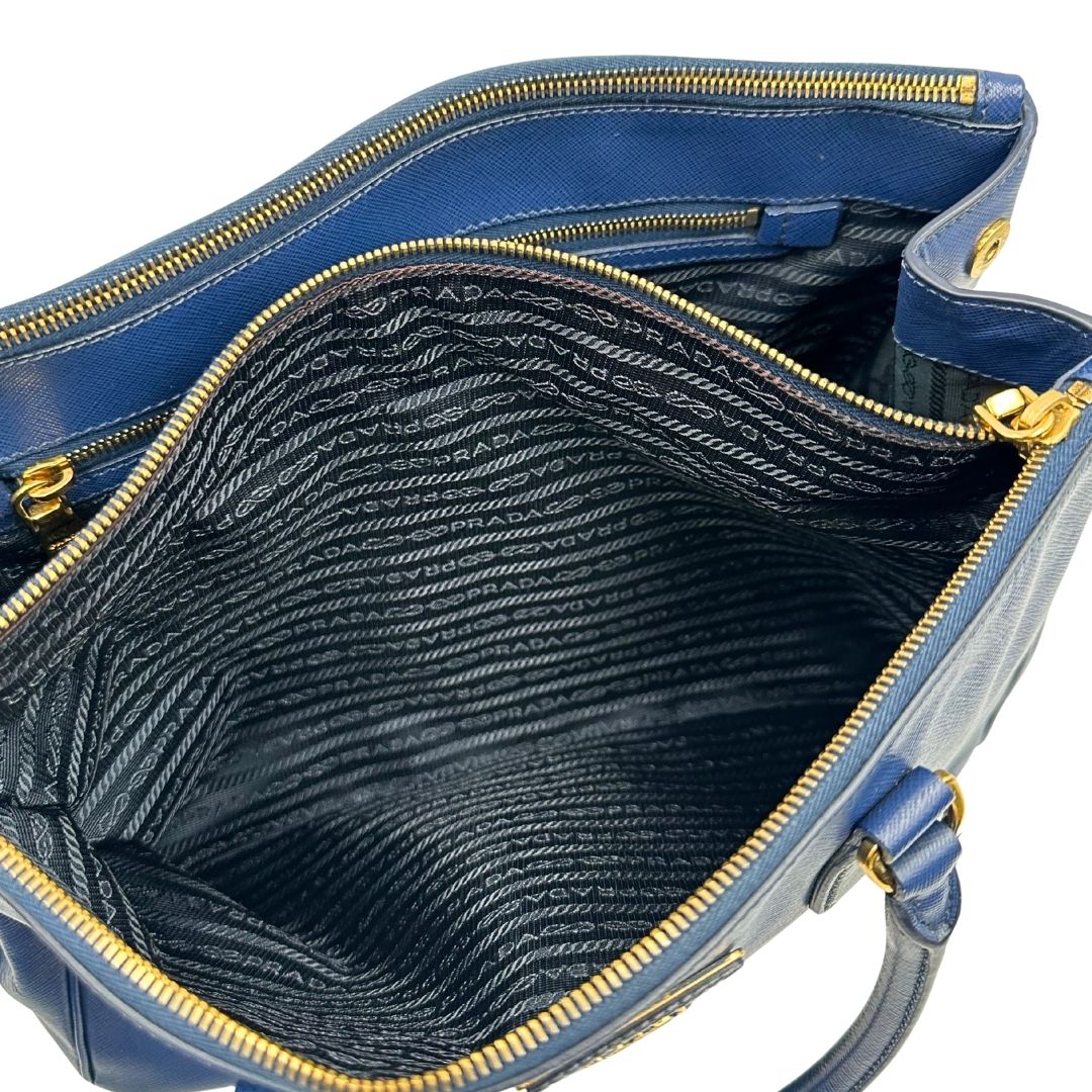 interno Borsa Prada in pelle saffiano blu con parti metalliche dorate; munita di doppi manici stondati e impreziosita da una clochette portachiavi, di lusso, originale, ottime condizioni. 