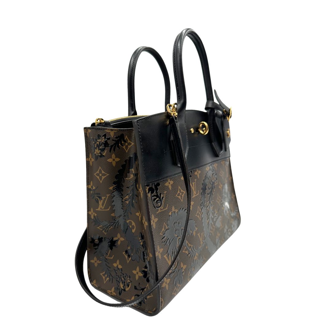lato Borsa Louis Vuitton L.E. in canvas marrone monogram con finiture in pelle nera e parti metalliche dorate, impreziosita da motivo decorativo floreale verniciato nero e un porta address amovibile; munita di doppi manici stondati e una tracolla amovibile. Completa di dustbag, di lusso, originale, ottime condizioni. 