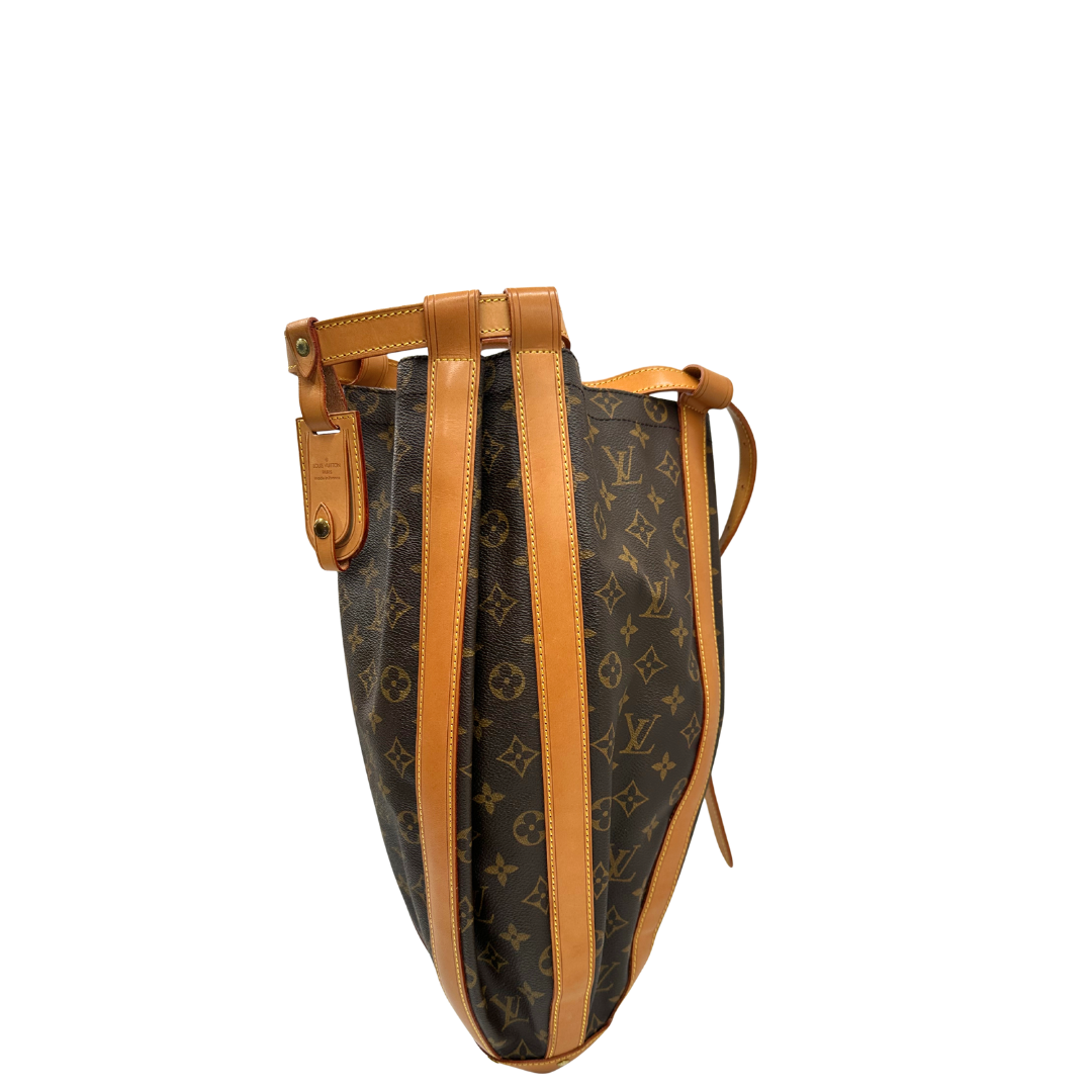 Lato sinistro di un Zaino Louis Vuitton in canvas marrone monogram con finiture in vacchetta naturale e parti metalliche dorate; munita di un cinturino centrale con fibbia e un manico amovibili. Indossabile a spalla. Completa di dustbag. Originale, usata, di lusso, in ottime condizioni.