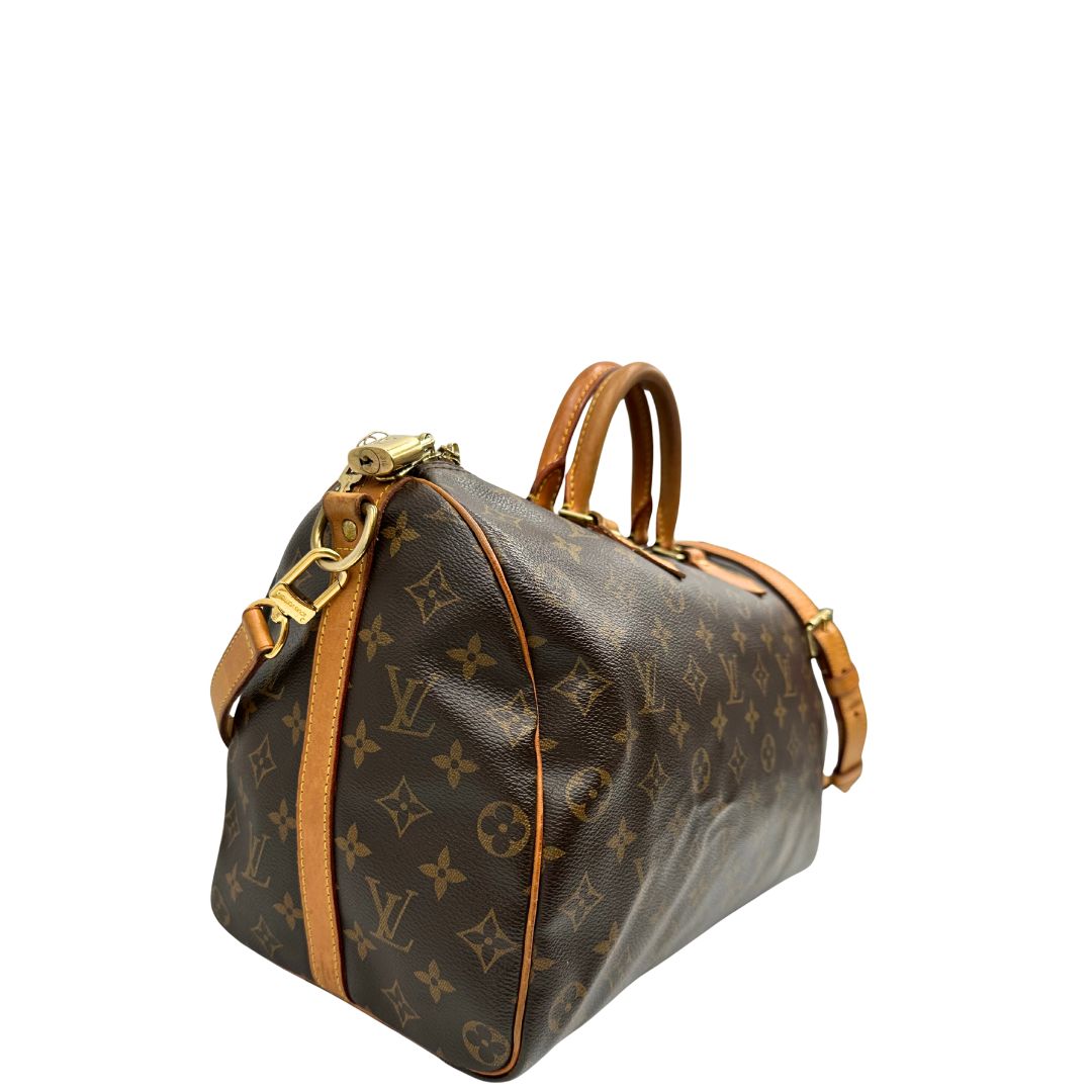 Lato destro di una Borsa Speedy 35 in canvas marrone monogram con finiture in vacchetta naturale e parti metalliche dorate; munita di doppi manici stondati e una tracolla amovibile e regolabile. Completa di lucchetto e chiavi. Originale, usato, di lusso, in ottime condizioni.