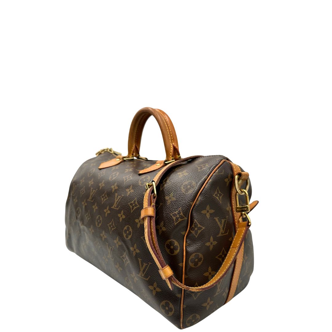 Lato sinistro di una Borsa Speedy 35 in canvas marrone monogram con finiture in vacchetta naturale e parti metalliche dorate; munita di doppi manici stondati e una tracolla amovibile e regolabile. Completa di lucchetto e chiavi. Originale, usato, di lusso, in ottime condizioni.