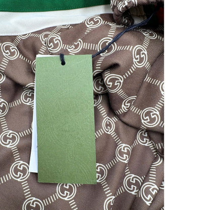 Pantalone tuta Gucci elasticizzato modello Interlocking G in 55% poliestere e 45% cotone, marrone e avorio con motivo GG all-over e bande laterali con bottoni automatici che si aprono fino ai fianchi, con strisce Web verde/rosse.