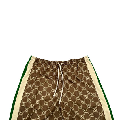 Pantalone tuta Gucci elasticizzato modello Interlocking G in 55% poliestere e 45% cotone, marrone e avorio con motivo GG all-over e bande laterali con bottoni automatici che si aprono fino ai fianchi, con strisce Web verde/rosse.