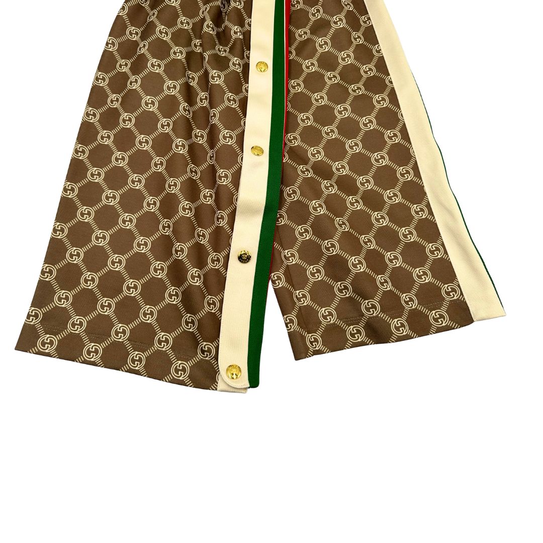 Pantalone tuta Gucci elasticizzato modello Interlocking G in 55% poliestere e 45% cotone, marrone e avorio con motivo GG all-over e bande laterali con bottoni automatici che si aprono fino ai fianchi, con strisce Web verde/rosse.