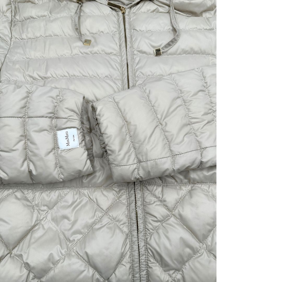 Piumino Max Mara The Cube in 100% poliammide trapuntato, colore avorio perla. Modello con cappuccio, coulisse regolabile in vita e dettagli metallici dorati. Chiusura con zip.