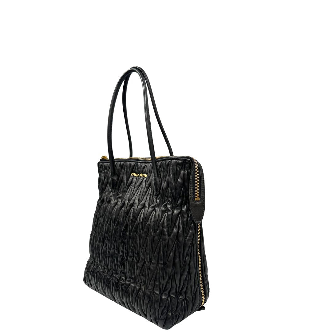 Lato sinistro di una Borsa Miu Miu realizzata in pelle goffrata nera con parti metalliche dorate; munita di due manici stondati, indossabile a spalla. Originale,, usata, di lusso, in ottime condizioni.
