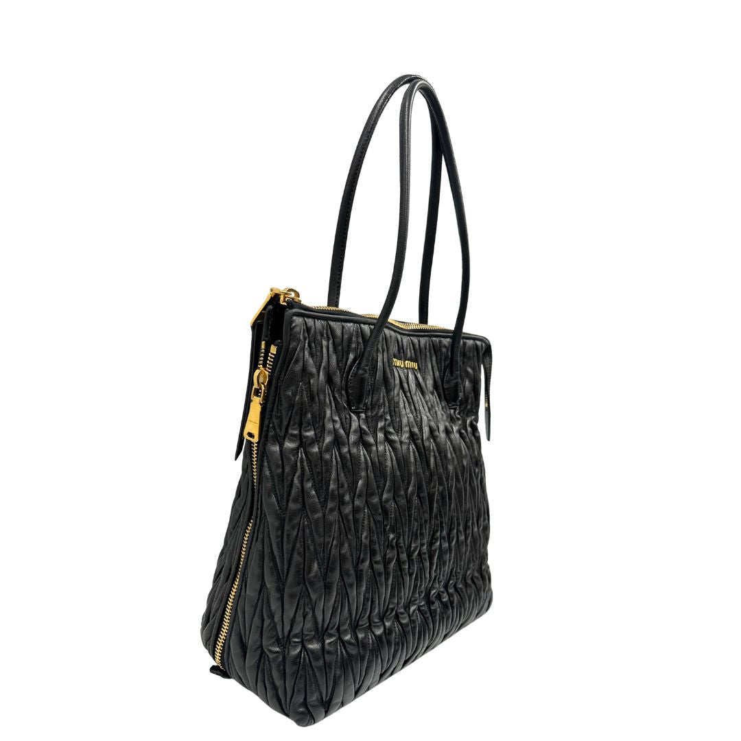 Lato destro di un Borsa Miu Miu realizzata in pelle goffrata nera con parti metalliche dorate; munita di due manici stondati, indossabile a spalla. Originale,, usata, di lusso, in ottime condizioni.