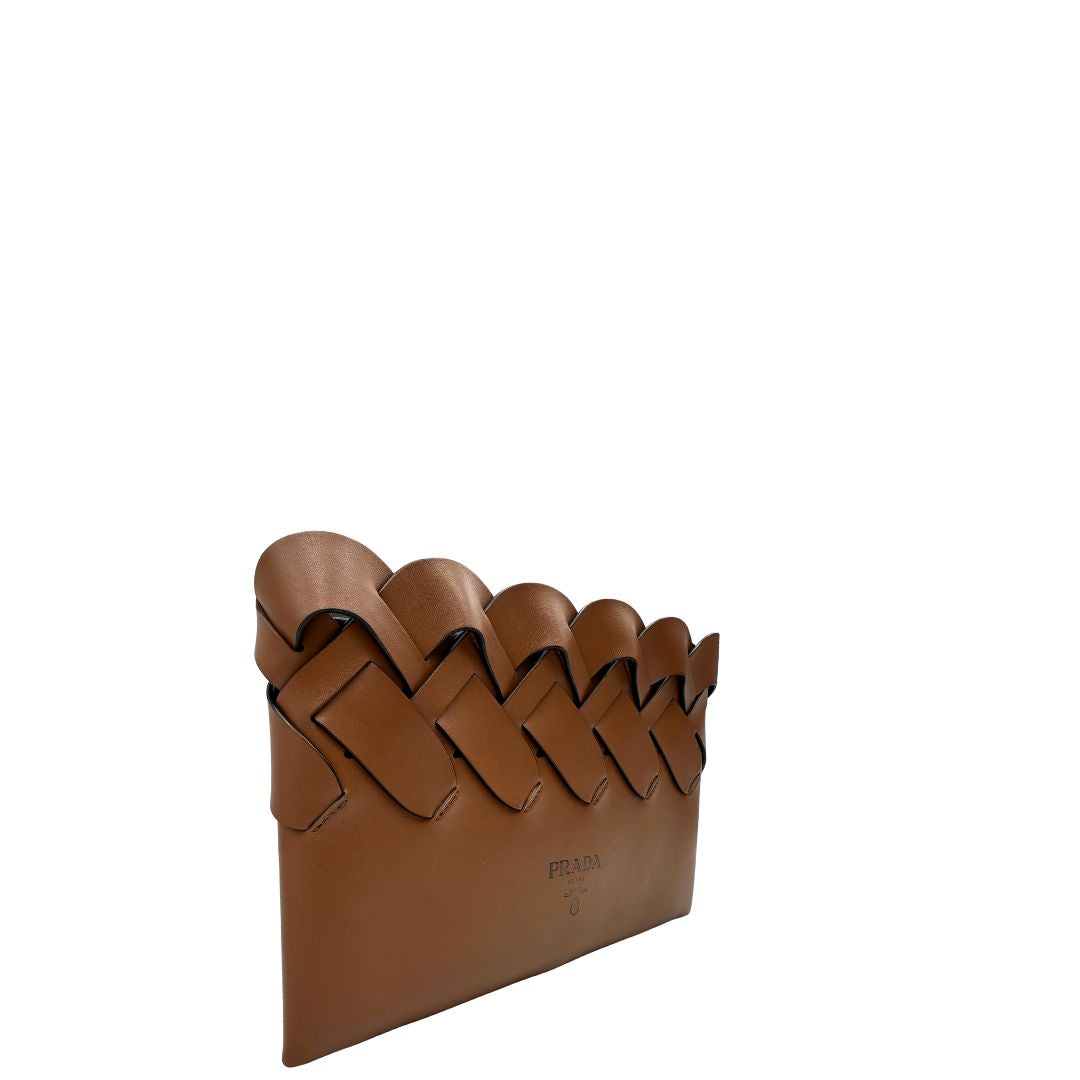 Lato destro di una Pochette Prada in pelle marrone cognac con parti metalliche argentate, presenta un motivo intrecciato nella parte superiore, munita di una pochette estraibile in pelle nera con logo lettering sul front. Originale, usata, di lusso, in ottime condizioni.