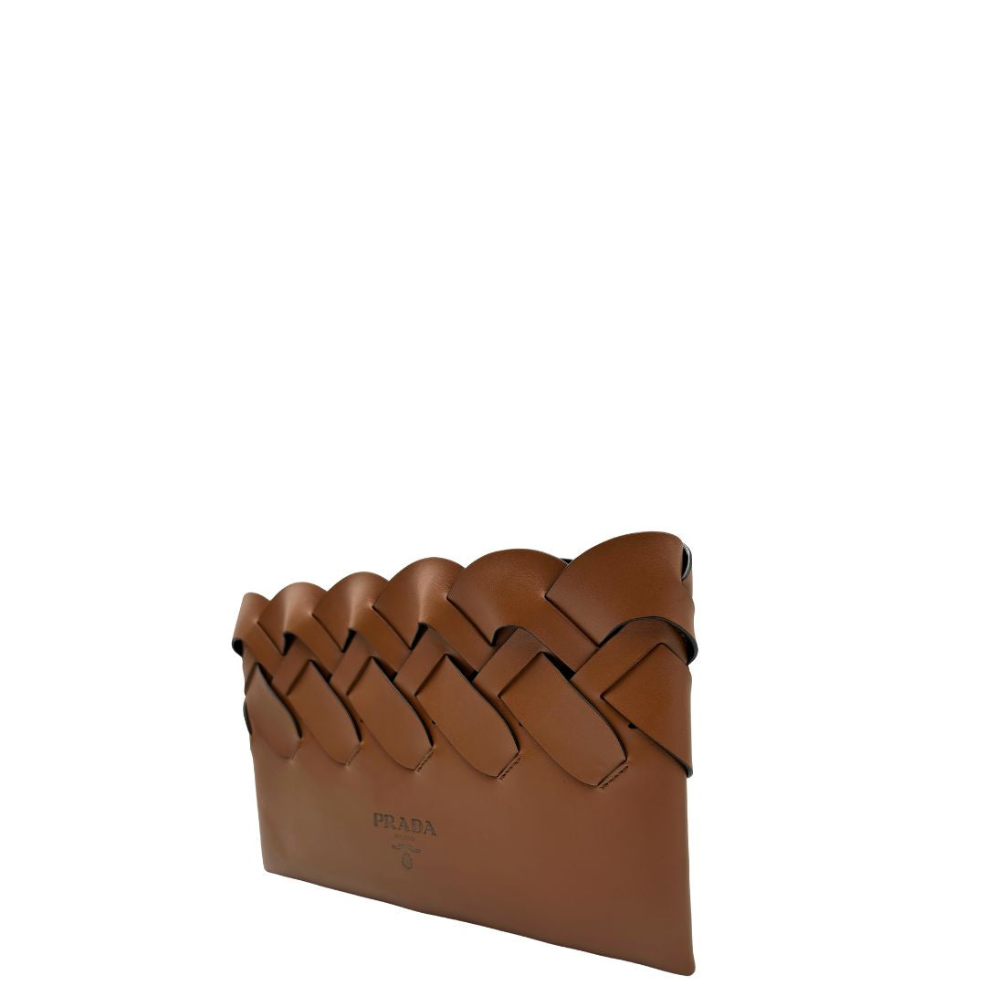 Lato sinistro di una Pochette Prada in pelle marrone cognac con parti metalliche argentate, presenta un motivo intrecciato nella parte superiore, munita di una pochette estraibile in pelle nera con logo lettering sul front. Originale, usata, di lusso, in ottime condizioni.