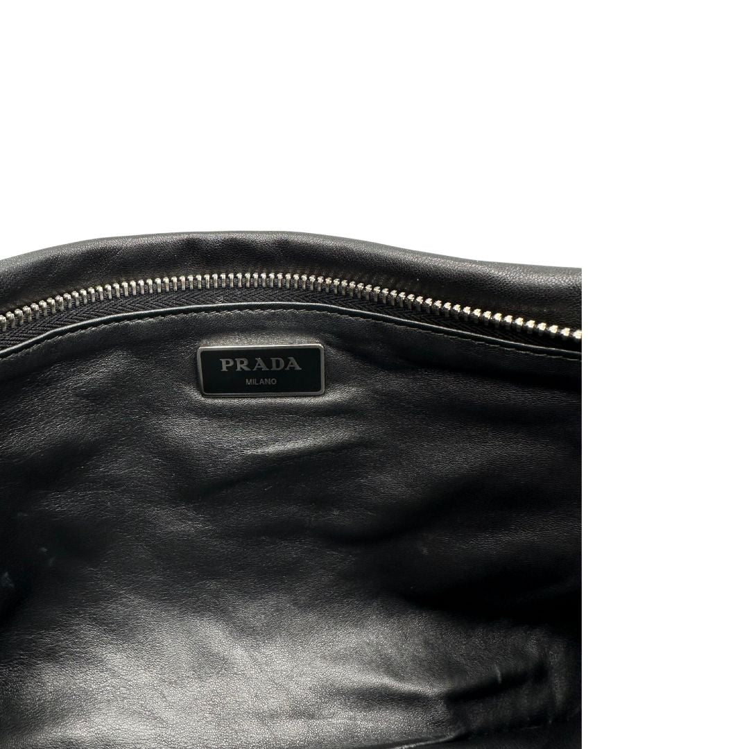 Interno di una Pochette Prada in pelle marrone cognac con parti metalliche argentate, presenta un motivo intrecciato nella parte superiore, munita di una pochette estraibile in pelle nera con logo lettering sul front. Originale, usata, di lusso, in ottime condizioni.