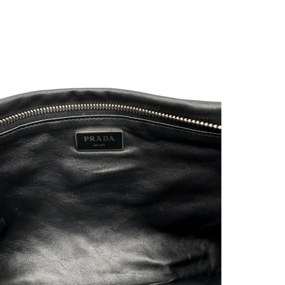Interno di una Pochette Prada in pelle marrone cognac con parti metalliche argentate, presenta un motivo intrecciato nella parte superiore, munita di una pochette estraibile in pelle nera con logo lettering sul front. Originale, usata, di lusso, in ottime condizioni.