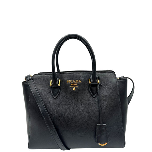 Front di una Borsa Prada in pelle saffiano nera con parti metalliche dorate; munita di doppi manici stondati e una tracolla amovibile e regolabile. Indossabile a tracolla oppure a mano. Originale, usata, di lusso, in ottime condizioni.