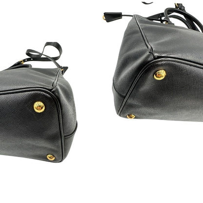 Angoli di una borsa Prada in pelle saffiano nera con parti metalliche dorate, munita di doppi manici stondati, tracolla amovibile e regolabile ed una clochette portachiavi. Completa di dustbag