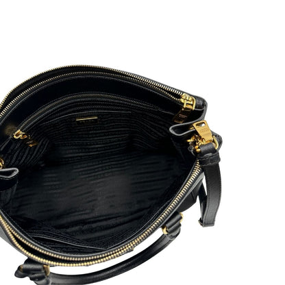 Interno di una borsa Prada in pelle saffiano nera con parti metalliche dorate, munita di doppi manici stondati, tracolla amovibile e regolabile ed una clochette portachiavi. Completa di dustbag