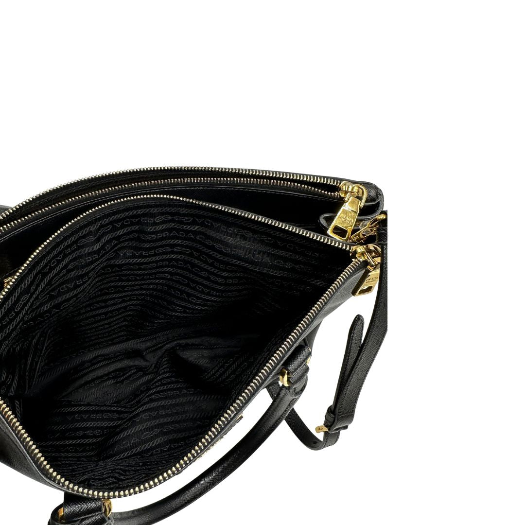 Interno di una borsa Prada in pelle saffiano nera con parti metalliche dorate, munita di doppi manici stondati, tracolla amovibile e regolabile ed una clochette portachiavi. Completa di dustbag