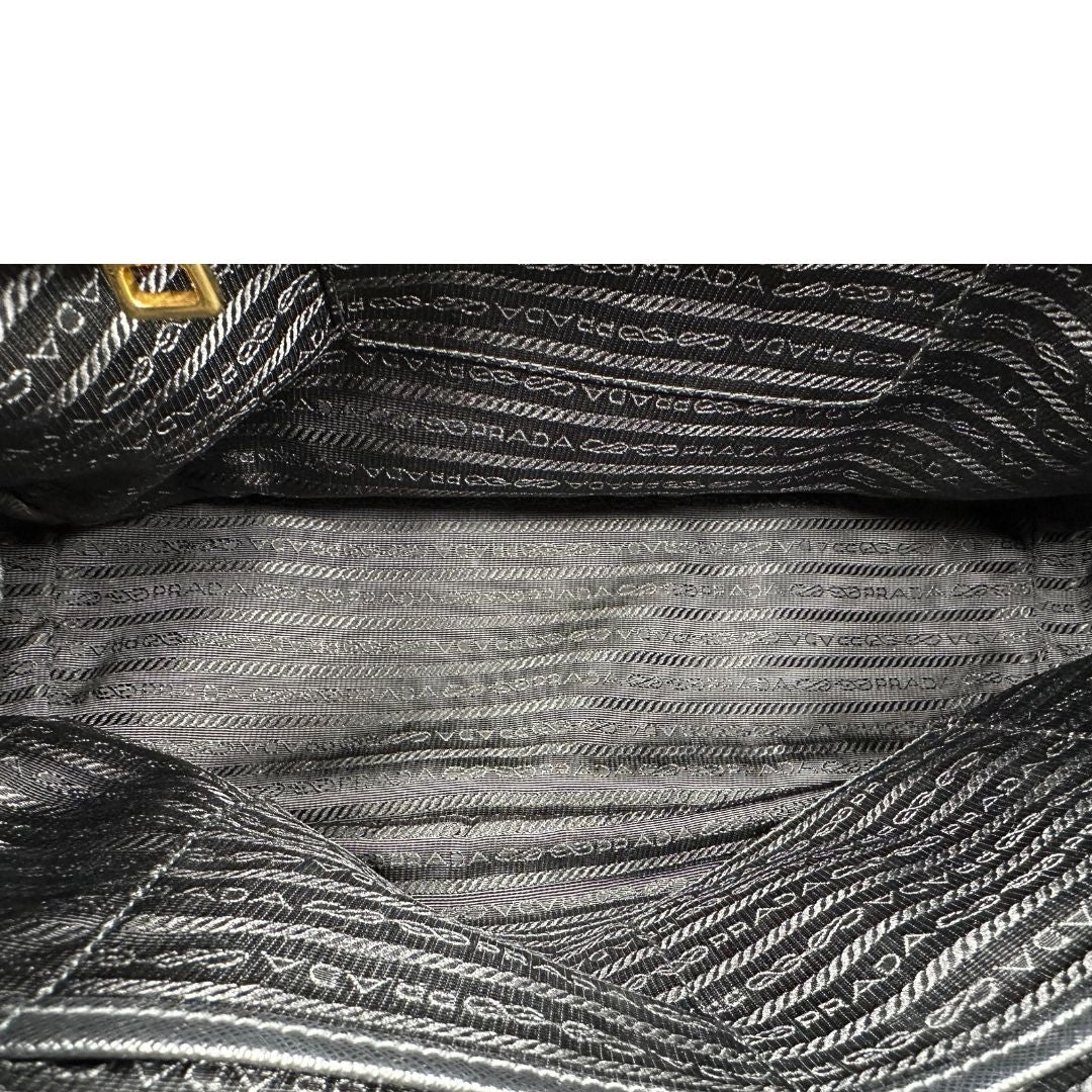 Interno di una borsa Prada in pelle saffiano nera con parti metalliche dorate, munita di doppi manici stondati, tracolla amovibile e regolabile ed una clochette portachiavi. Completa di dustbag