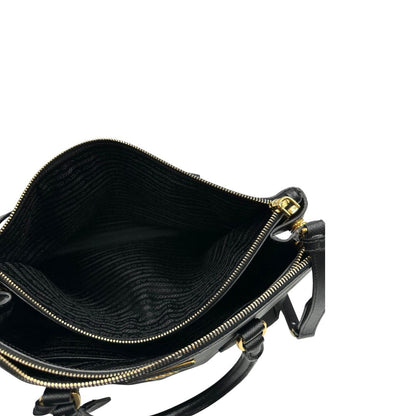 Interno di una borsa Prada in pelle saffiano nera con parti metalliche dorate, munita di doppi manici stondati, tracolla amovibile e regolabile ed una clochette portachiavi. Completa di dustbag
