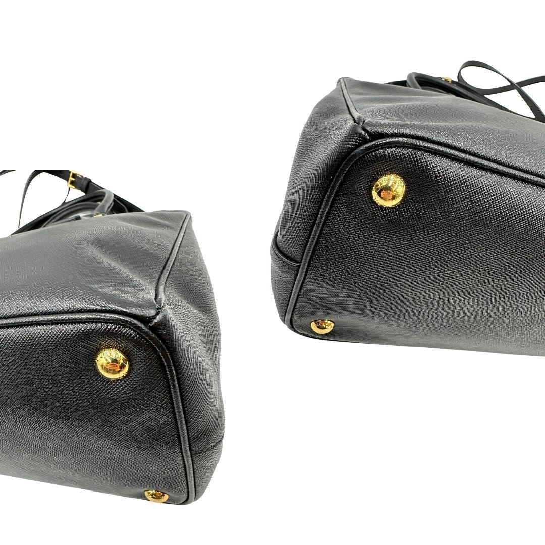 Angoli di una borsa Prada in pelle saffiano nera con parti metalliche dorate, munita di doppi manici stondati, tracolla amovibile e regolabile ed una clochette portachiavi. Completa di dustbag