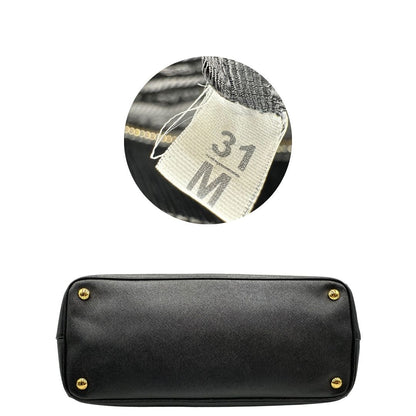 Base e codice di una borsa Prada in pelle saffiano nera con parti metalliche dorate, munita di doppi manici stondati, tracolla amovibile e regolabile ed una clochette portachiavi. Completa di dustbag