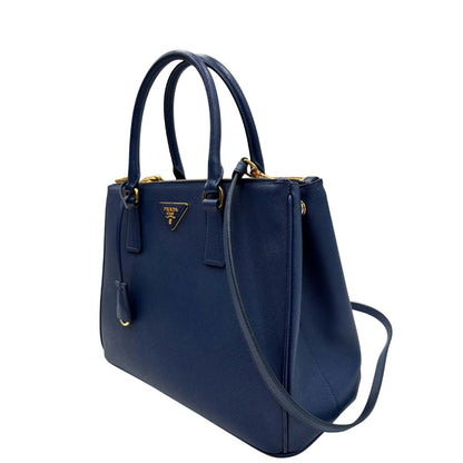 lato Borsa Prada in pelle saffiano blu con parti metalliche dorate; munita di doppi manici stondati, una tracolla amovibile e regolabile e impreziosita da un portachiavi, usata, originale, ottime condizioni. 