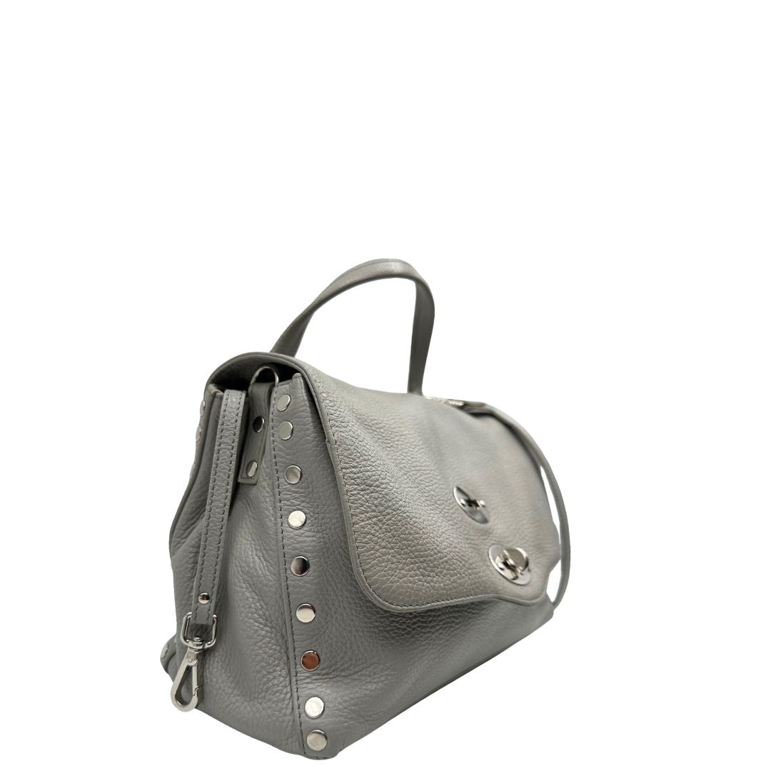 Laterale sinistro di una borsa Zanellato in pelle martellata grigio chiaro, parti con metalliche argentate; munita di un manico singolo, tracolla amovibile e regolabile. Completa di dustbag.