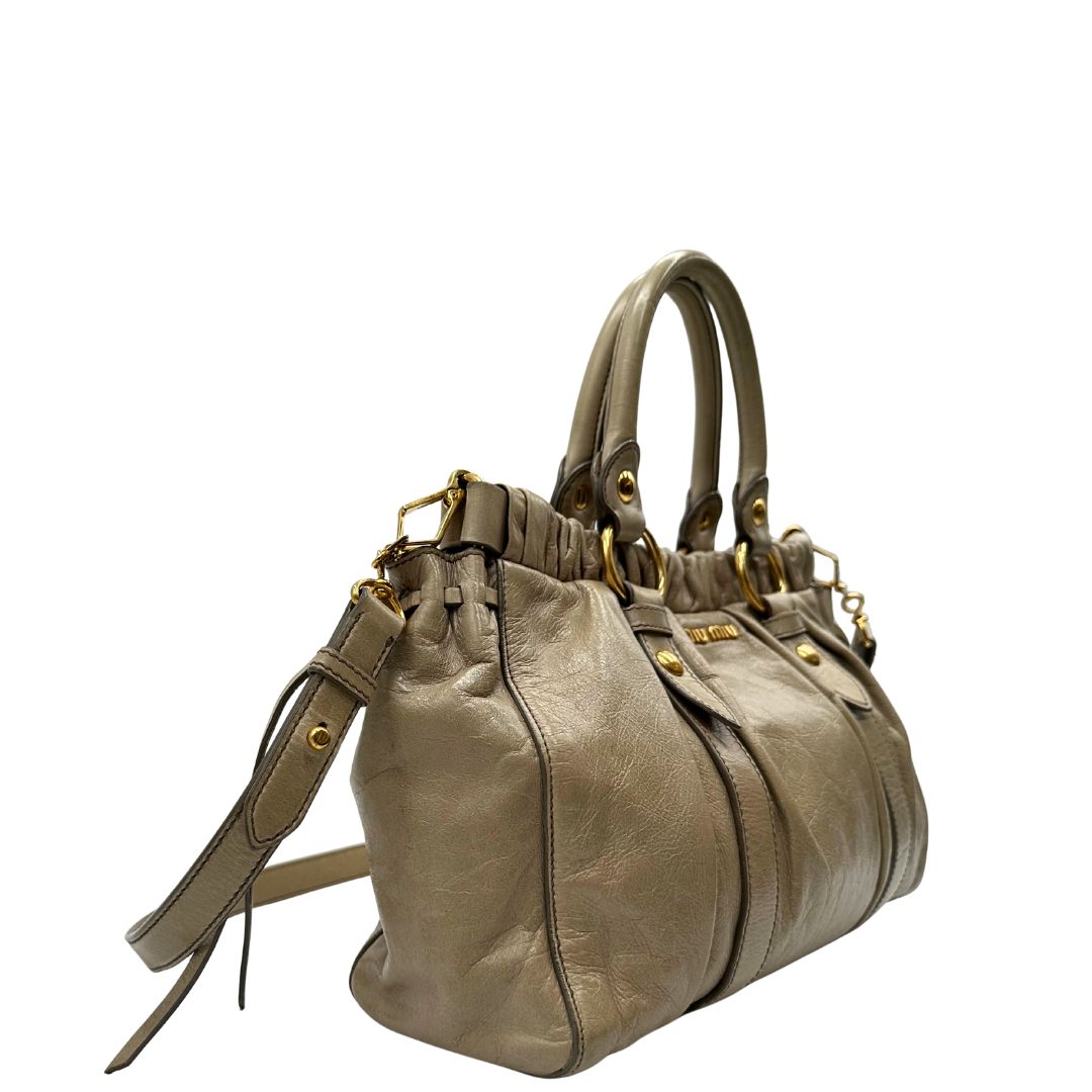lato Borsa Miu Miu in pelle beige con parti metalliche dorate; munita di una tracolla e doppi manici stondati. Completa di dustbag, di lusso, originale, ottime condizioni. 
