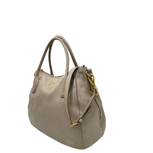 Lato sinistro di una Borsa Tote Prada in pelle martellata color greige con parti metalliche dorate; munita di doppi manici stondati, una tracolla regolabile e amovibile. Originale, usata, di lusso, in ottime condizioni.