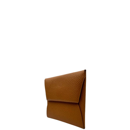 Laterale destro di un mini portamonete Hermès in pelle color cammello, con chiusura a bottone. Completo di scatola.