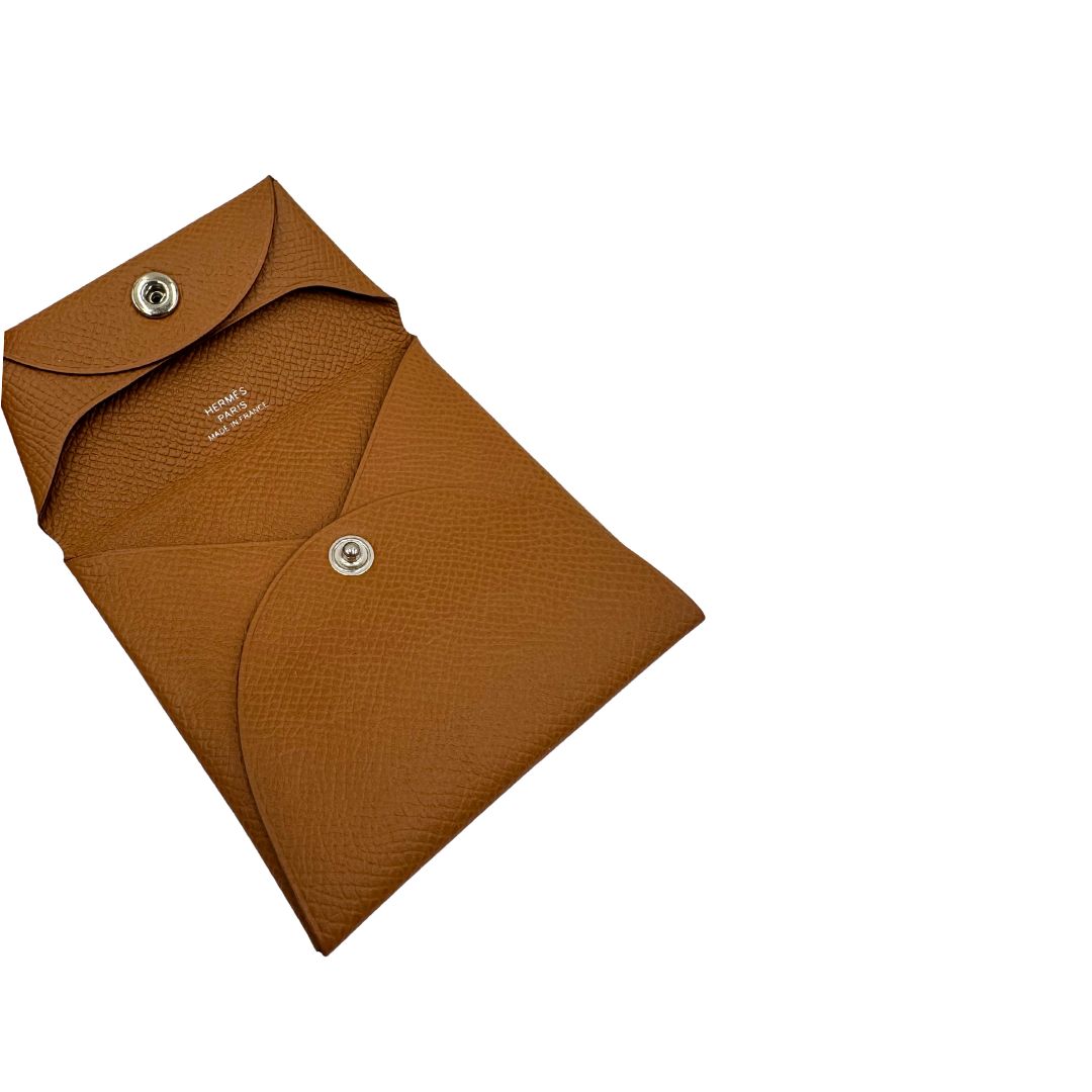 Apertura di un mini portamonete Hermès in pelle color cammello, con chiusura a bottone. Completo di scatola.