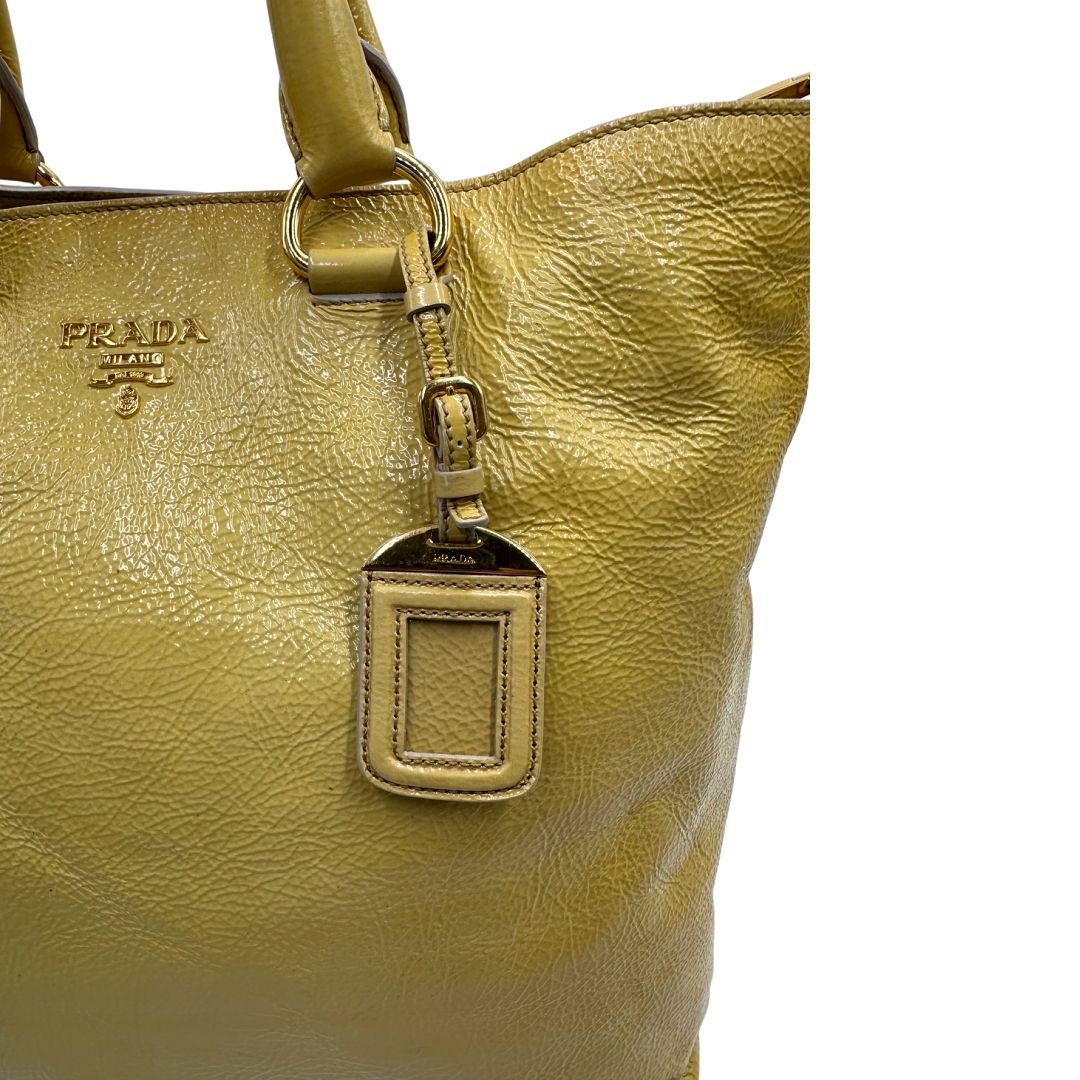 Borsa Prada in pelle lucida color mustard con parti metalliche dorate; munita di un accessorio porta address e doppi manici stondati. Indossabile a mano oppure a tracolla. Originale, usata, di lusso, in ottime condizioni
