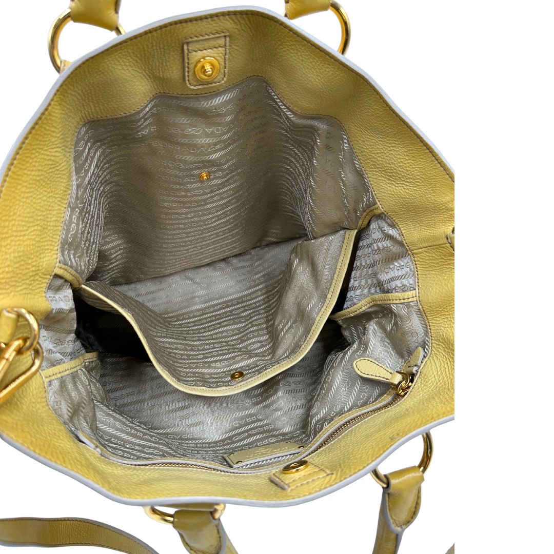 Interno di una Borsa Prada in pelle lucida color mustard con parti metalliche dorate; munita di un accessorio porta address e doppi manici stondati. Indossabile a mano oppure a tracolla. Originale, usata, di lusso, in ottime condizioni