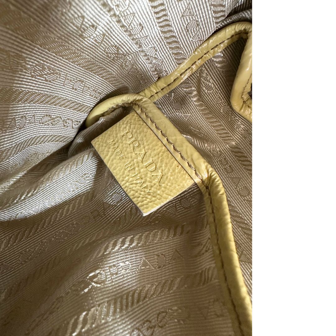 Interno di una Borsa Prada in pelle lucida color mustard con parti metalliche dorate; munita di un accessorio porta address e doppi manici stondati. Indossabile a mano oppure a tracolla. Originale, usata, di lusso, in ottime condizioni