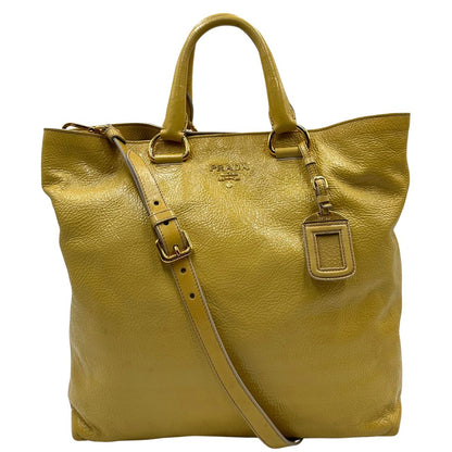 Front di una Borsa Prada in pelle lucida color mustard con parti metalliche dorate; munita di un accessorio porta address e doppi manici stondati. Indossabile a mano oppure a tracolla. Originale, usata, di lusso, in ottime condizioni