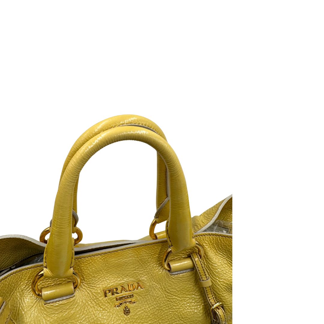 Manici di una Borsa Prada in pelle lucida color mustard con parti metalliche dorate; munita di un accessorio porta address e doppi manici stondati. Indossabile a mano oppure a tracolla. Originale, usata, di lusso, in ottime condizioni