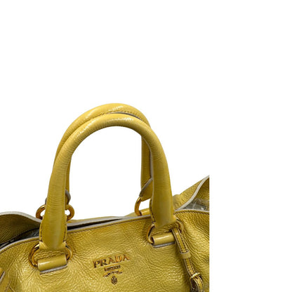 Manici di una Borsa Prada in pelle lucida color mustard con parti metalliche dorate; munita di un accessorio porta address e doppi manici stondati. Indossabile a mano oppure a tracolla. Originale, usata, di lusso, in ottime condizioni