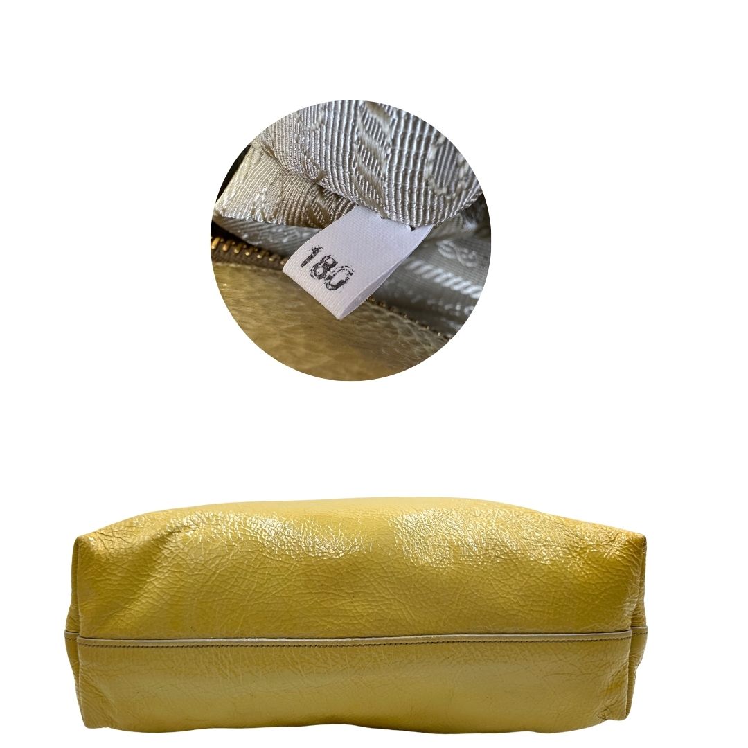 Base e codice di una Borsa Prada in pelle lucida color mustard con parti metalliche dorate; munita di un accessorio porta address e doppi manici stondati. Indossabile a mano oppure a tracolla. Originale, usata, di lusso, in ottime condizioni