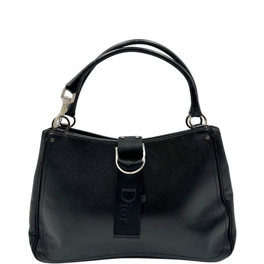  Front di una Borsa Dior in pelle nera con parti metalliche argentate; caratterizzata da una chiusura con cinturino centrale in tessuto con logo Dior tono su tono, dotata di due manici stondati con gancio decorativo impreziosito da cristalli. Completa di dustbag. Originale, usata, di lusso, in ottime condizioni.