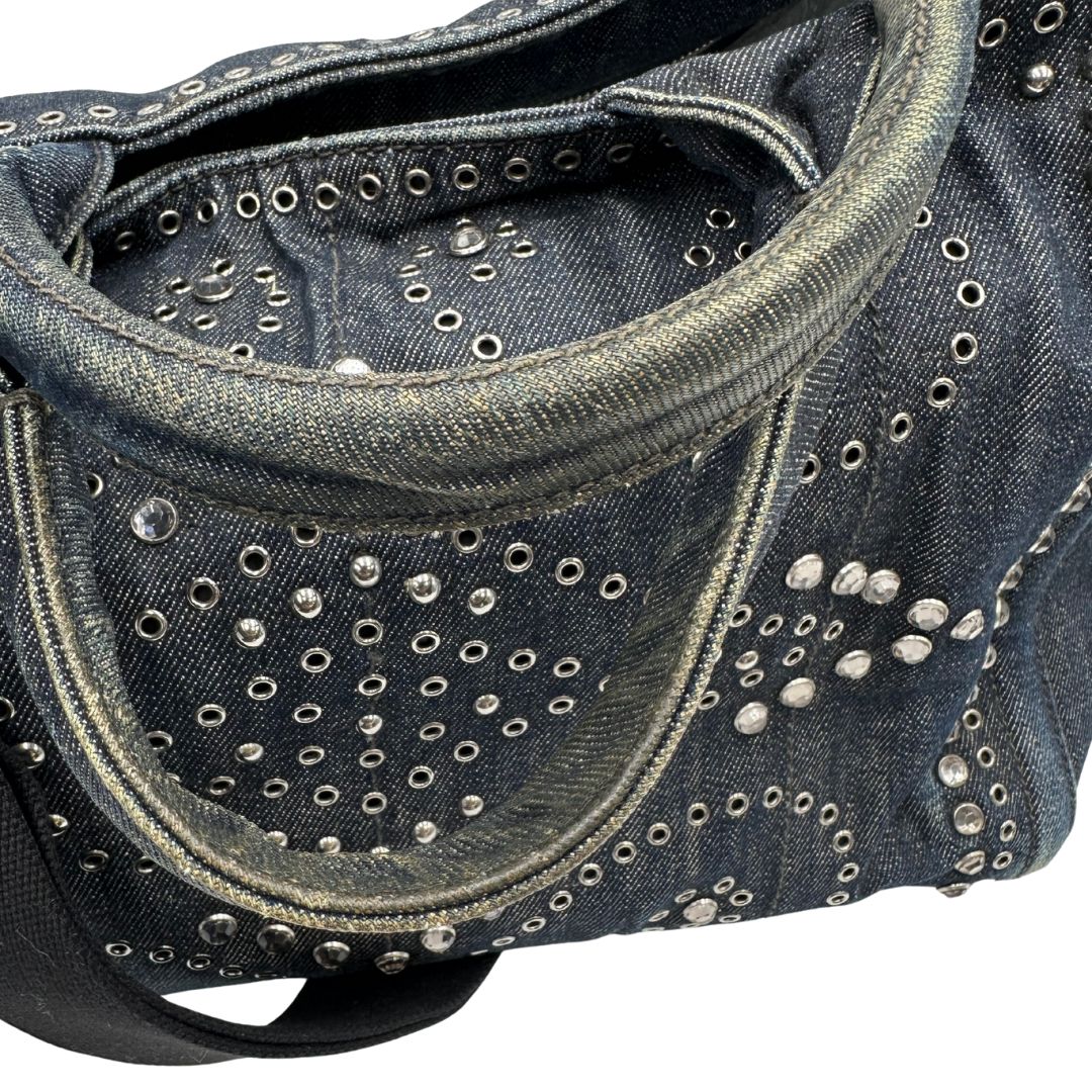 manici Borsa Prada in denim blu rifinita con borchie metalliche argentate; munita di una tracolla in tessuto regolabile e amovibile e doppi manici; indossabile a mano o a tracolla. Completa di dustbag, di lusso, originale, buone condizioni.