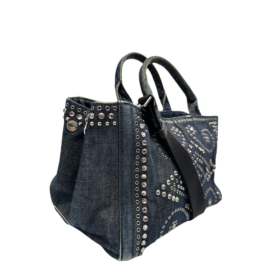 lato Borsa Prada in denim blu rifinita con borchie metalliche argentate; munita di una tracolla in tessuto regolabile e amovibile e doppi manici; indossabile a mano o a tracolla. Completa di dustbag, di lusso, originale, buone condizioni. 