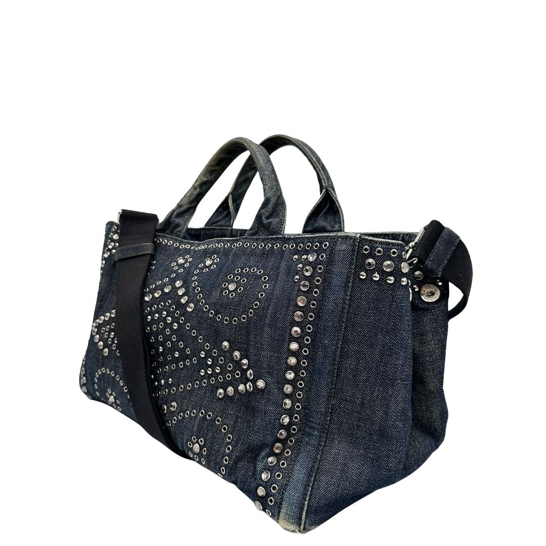 lato Borsa Prada in denim blu rifinita con borchie metalliche argentate; munita di una tracolla in tessuto regolabile e amovibile e doppi manici; indossabile a mano o a tracolla. Completa di dustbag, di lusso, originale, buone condizioni. 