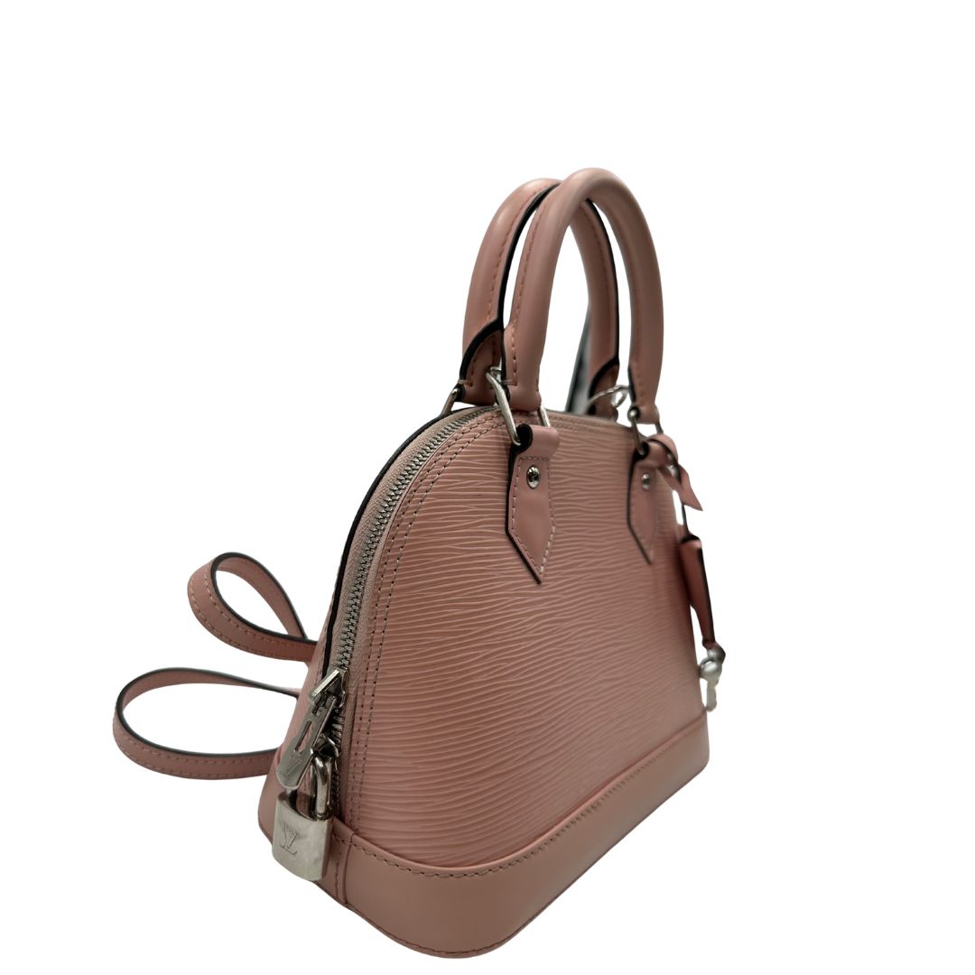 lato Borsa Louis Vuitton Alma BB in pelle epi rosa con parti metalliche argentate. Munita di doppi manici stondati e tracolla amovibile, dotata di clochette porta chiavi. Completa di lucchetto e chiavi, di lusso, originale, ottime condizioni. 