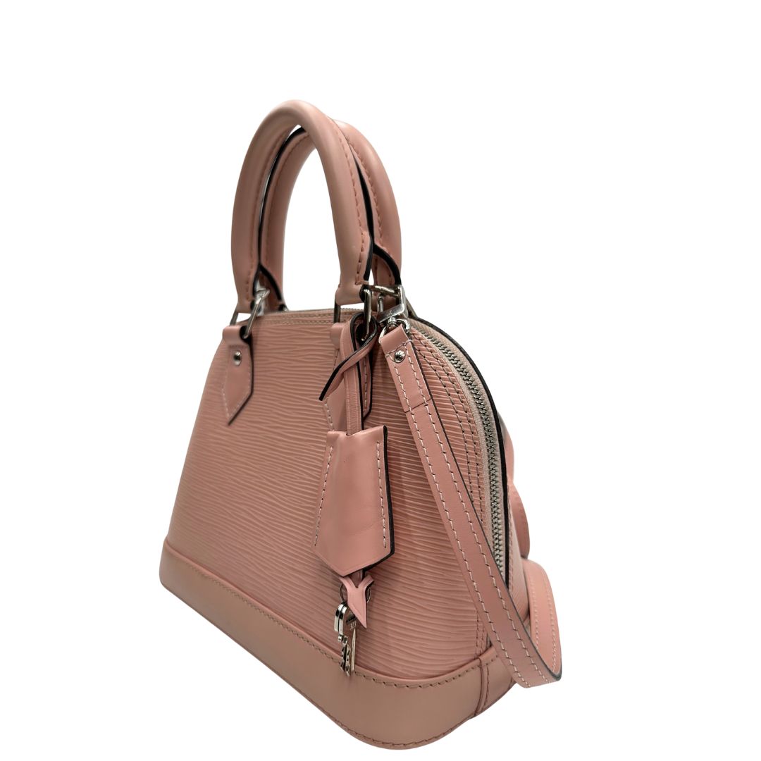 lato Borsa Louis Vuitton Alma BB in pelle epi rosa con parti metalliche argentate. Munita di doppi manici stondati e tracolla amovibile, dotata di clochette porta chiavi. Completa di lucchetto e chiavi, di lusso, originale, ottime condizioni. 