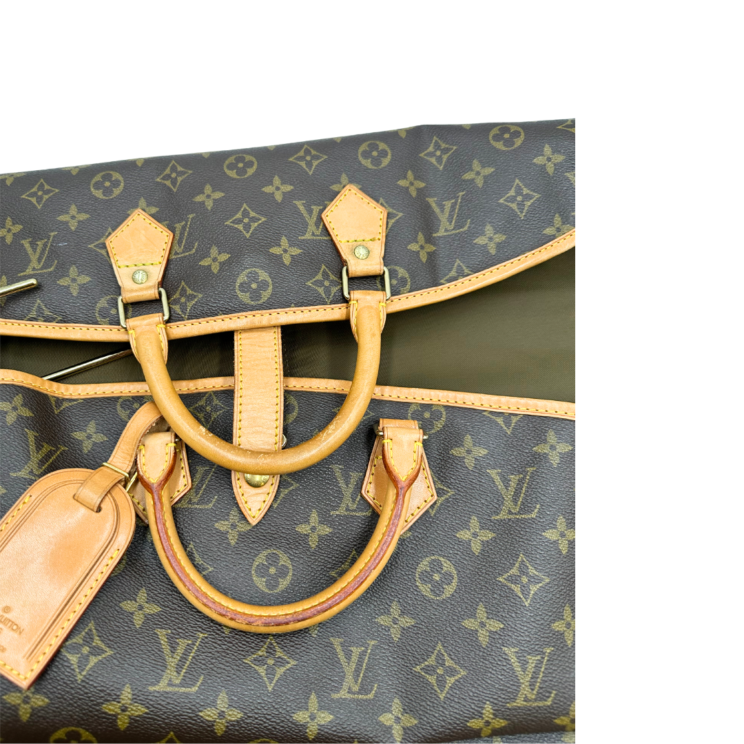 Manici di un Porta abiti in canvas marrone monogram con finiture in vacchetta naturale e parti metalliche dorate; munita di due manici stondati. Completa di due lucchetto, chiavi, tag porta address e una dustbag. Originale, usata, di lusso, in ottime condizioni.