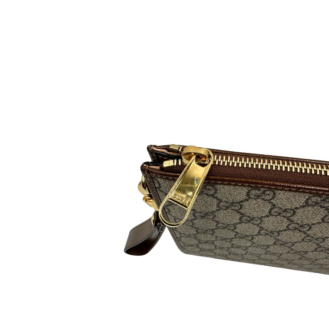 Chiusura di una Pochette Gucci in canvas GG monogram beige con finiture in pelle marroni e parti metalliche dorate; munita di un polsino in pelle amovibile, indossabile a mano. Originale, usata, di lusso, in ottime condizioni.