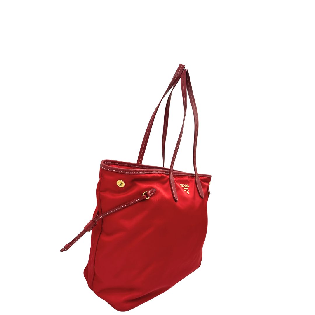 Lato destro di una Borsa Prada in nylon rosso con parti metalliche dorate e finiture in pelle tono su tono, munita di doppi manici, indossabile a spalla. Completa di dustbag. Originale, usata, di lusso, in ottime condizioni.