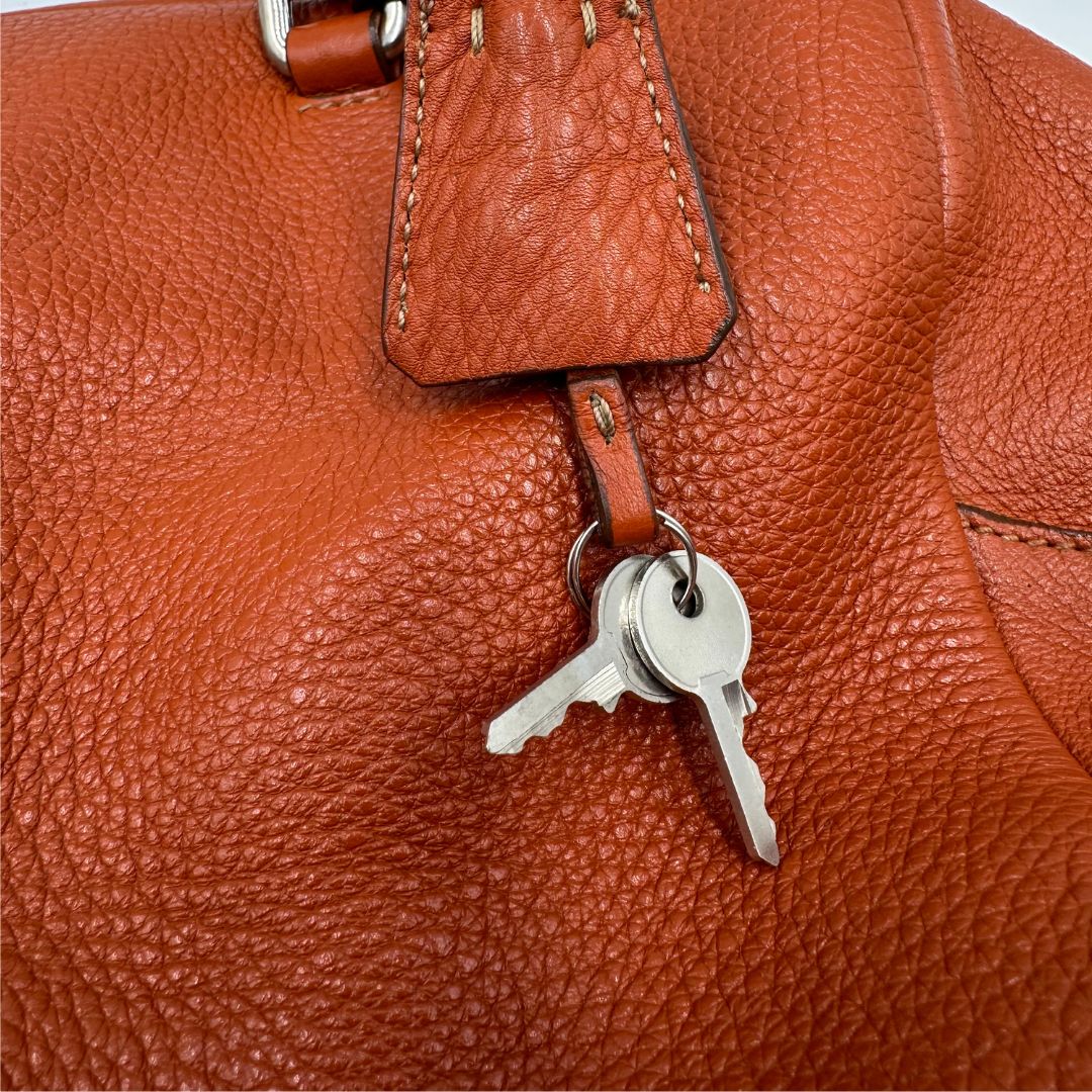 chiavi  Borsa Prada in pelle martellata color cognac con parti metalliche argentate; munita di doppi manici, indossabile a spalla. Completa di lucchetto e chiavi, di lusso, originale, ottime condizioni, usata. 