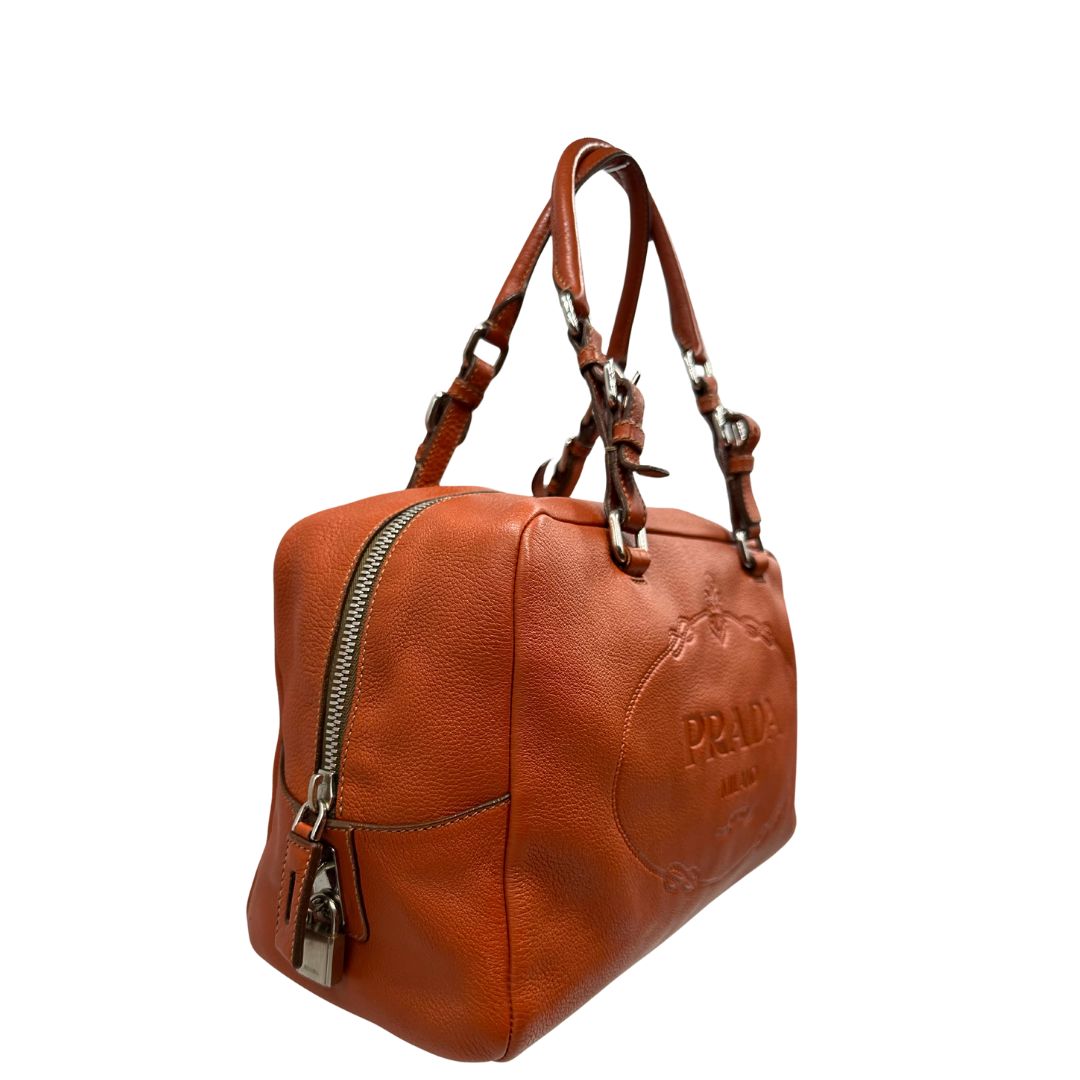 lato Borsa Prada in pelle martellata color cognac con parti metalliche argentate; munita di doppi manici, indossabile a spalla. Completa di lucchetto e chiavi, di lusso, originale, ottime condizioni, usata.