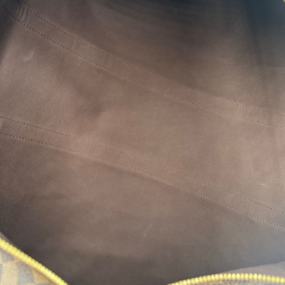 interno del Borsone Louis Vuitton in canvas Damier Ébène marrone con finiture in pelle tono su tono e parti metalliche dorate; munito di doppi manici stondati e una tracolla amovibile e regolabile. Completo di lucchetto, chiavi e dustbag, di lusso, originale, ottime condizioni, usato. 