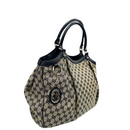 Lato destro di una Borsa Gucci in tessuto beige GG con parti metalliche dorate e parti in pelle color blu notte; munita di doppi manici stondati. Completa di dustbag. Originale, usata, di lusso, in ottime condizioni.